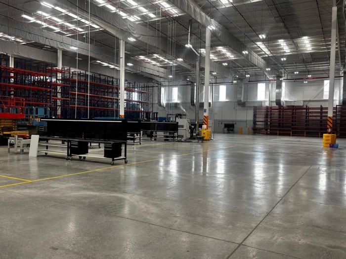 Piso de concreto pulido en nave industrial amplia, con racks de almacenamiento al fondo