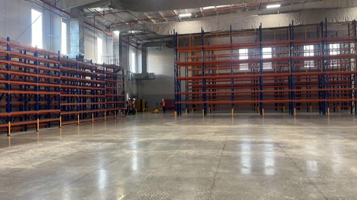 Pasillo de racks industriales naranja y azul iluminado por ventanales altos